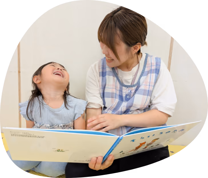 笑顔で絵本を読む保育士と園児
